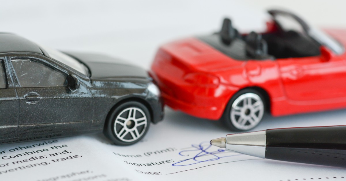 6 Ways To Reduce Your Car Insurance Rate A model of a car accident using two toy cars, red and black, on top of an insurance Insurance policy contract.