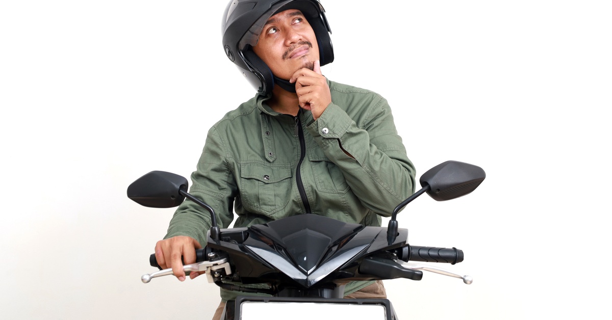 A man on a motorcycle is wearing a helmet and looking up with his hand on his chin. He's in front of a white background. A man on a motorcycle is wearing a helmet and looking up with his hand on his chin. He's in front of a white background.