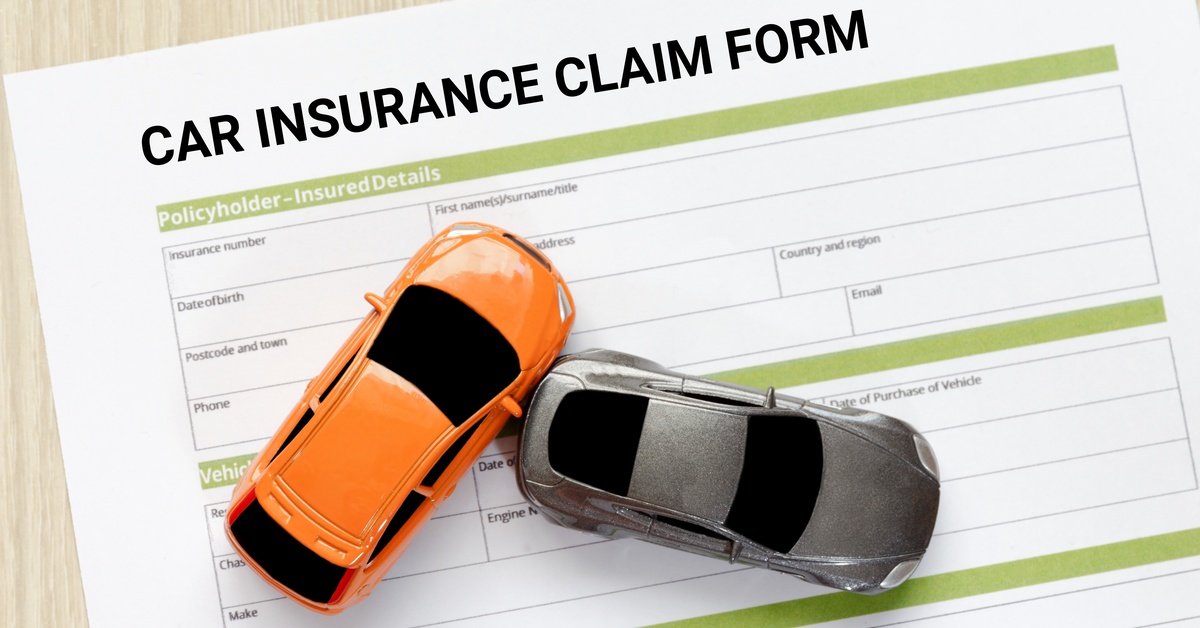 Two toy cars mimic a collision on top of a document that reads "car insurance claim form" on a wooden desk.