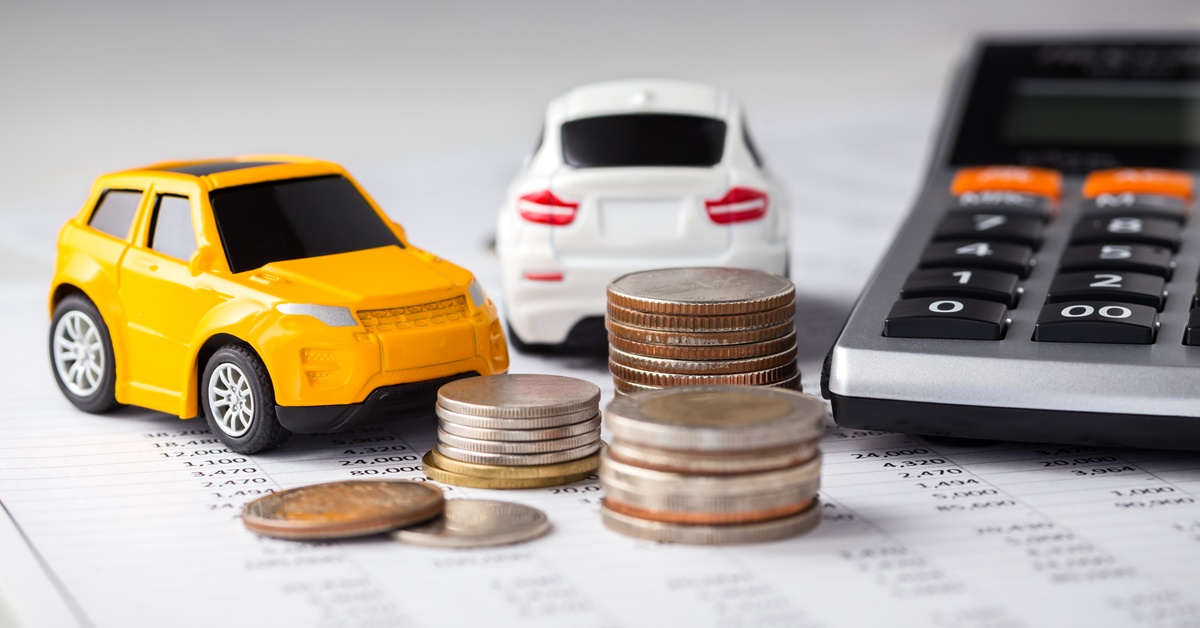 A close-up of two toy cars, stacks of coins, and a calculator on a sheet of paper that has rows of numbers.