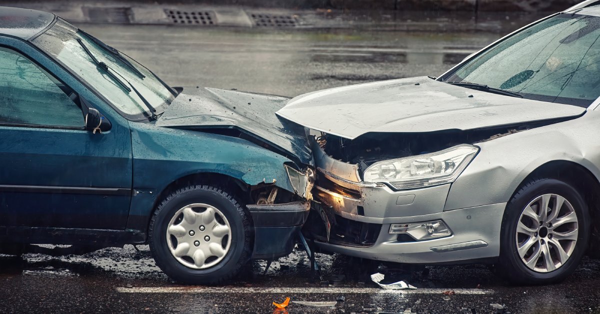 A moderate head-on vehicle collision between two sedans. There is debris on the ground in front of the vehicles.