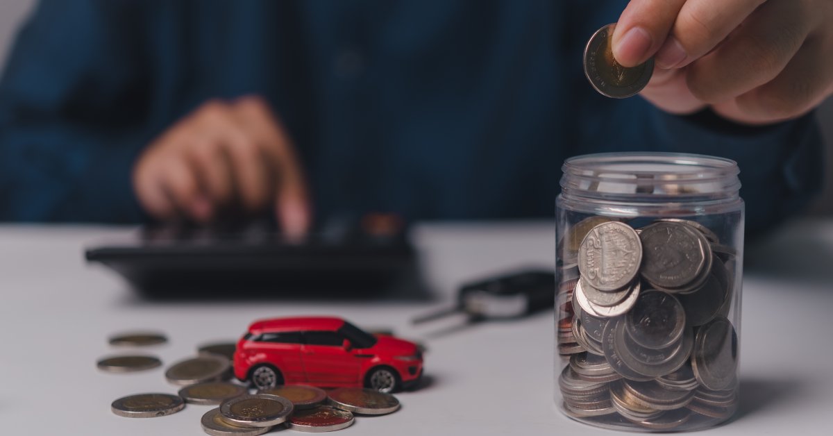 A person drops a quarter into a glass jar full of coins. A miniature red car sits in a pile of coins next to a car key.