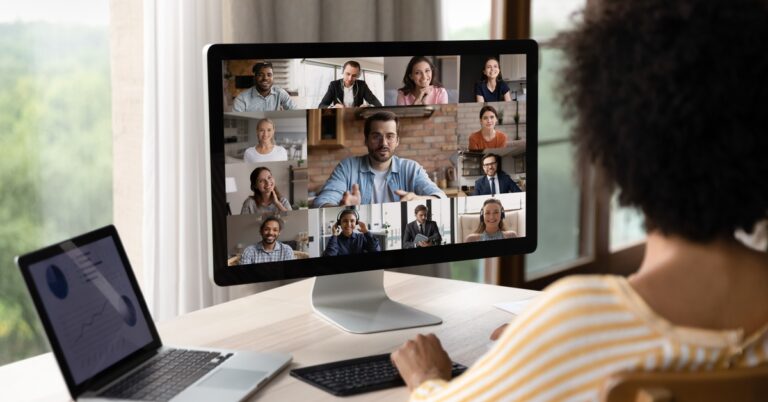 A person works at a desk, joining a video conference with multiple coworkers displayed on a computer screen.