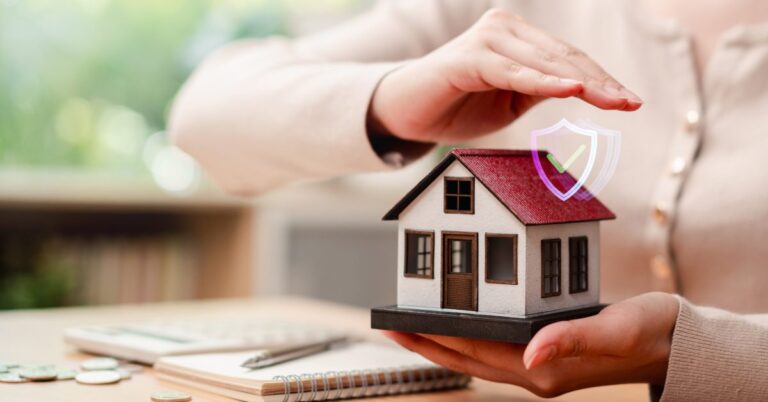A person holding a model house with a protective shield icon above it, symbolizing homeowners insurance coverage.